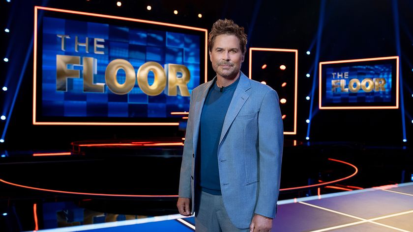 Rob Lowe standing on The Floor in a blue suit and tee and looking right at the camera before a taping.
