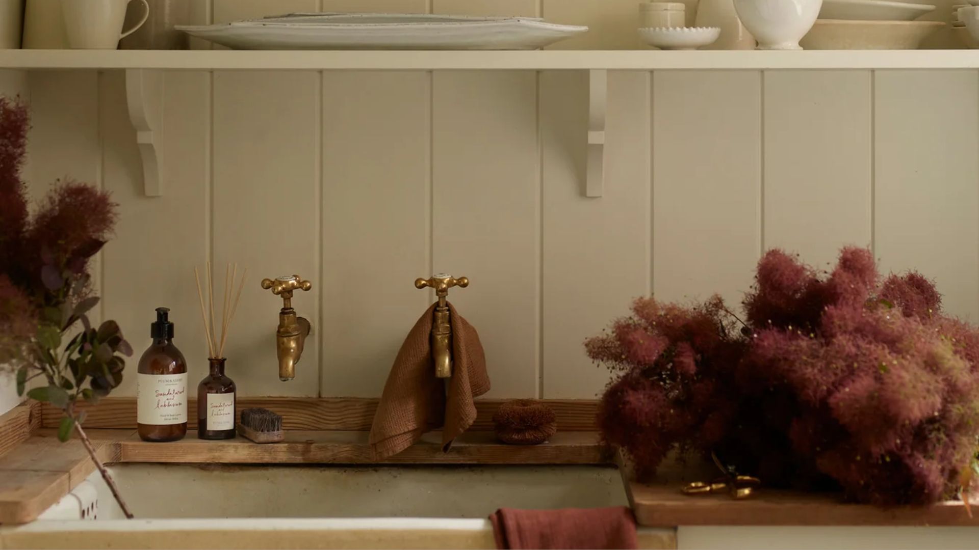 A kitchen sink with sprigs of feathered flowers, a reed diffuser and a refill bottle