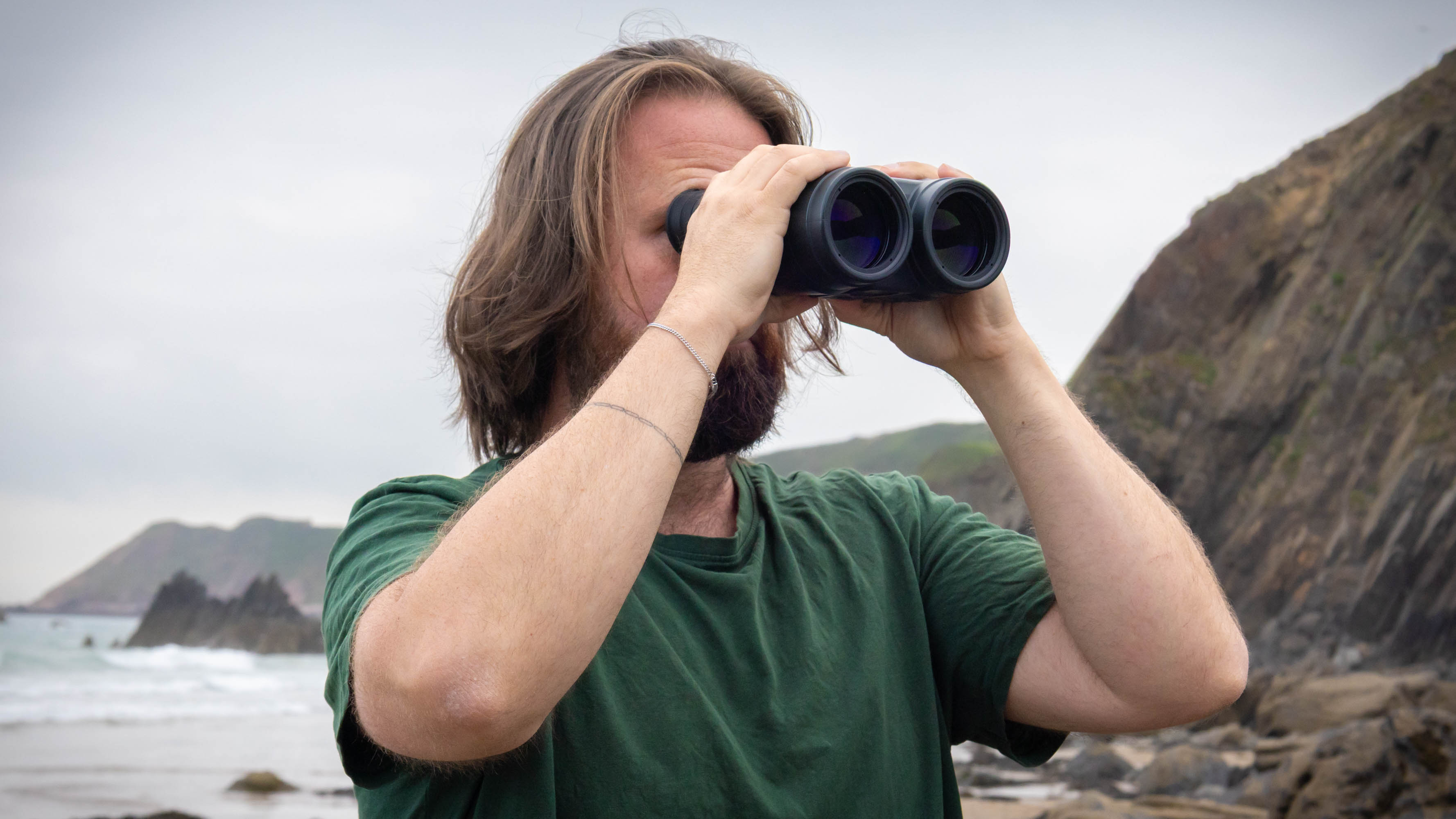 A male using the Canon 18x50 IS binoculars with the sea and coastline behind them.