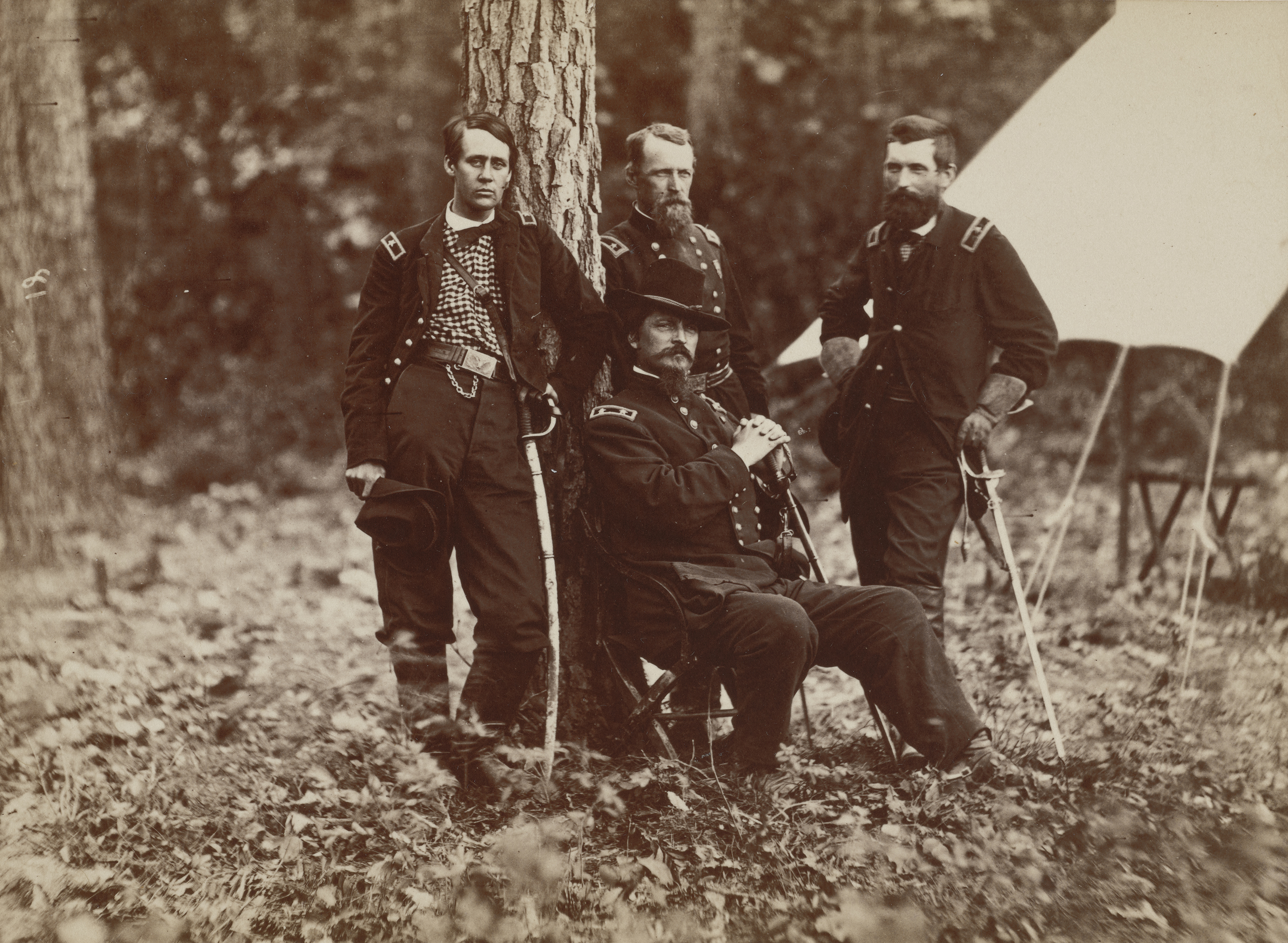 Four Union officers in formal uniforms, some carrying sabers, pose together in a wooded area near a white canvas tent.