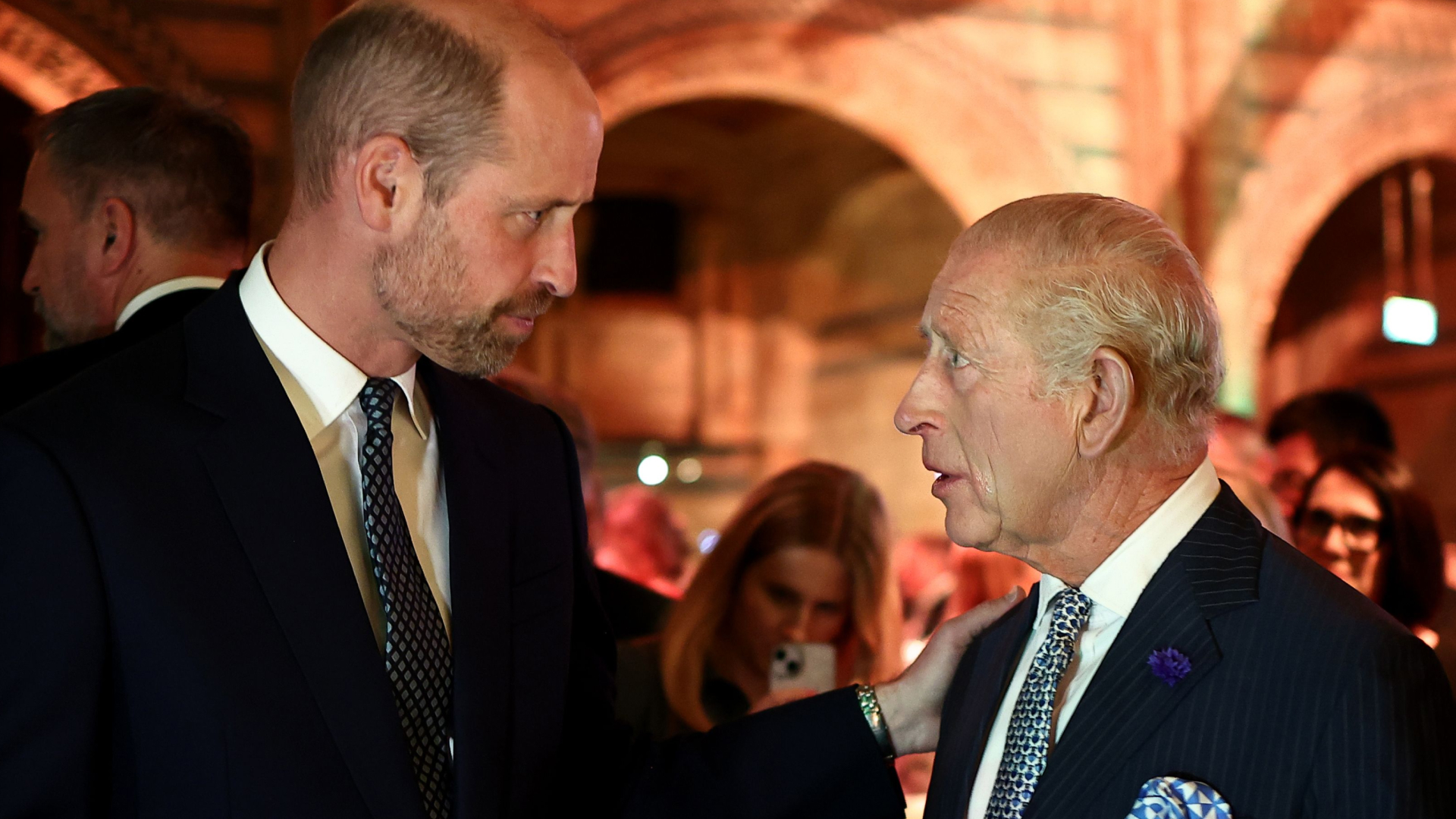 Prince William wears a suit and looks at his father King Charles