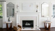 Image of a white living room wall that features wall molding. There is a fireplace in the center with two matching mirrors on either side of the fire place, each with a matching side table underneath.