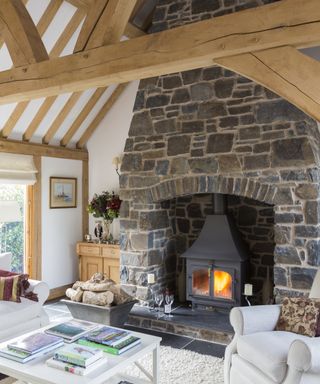 large stone inglenook fireplace with log burner in room with oak beams and vaulted ceiling