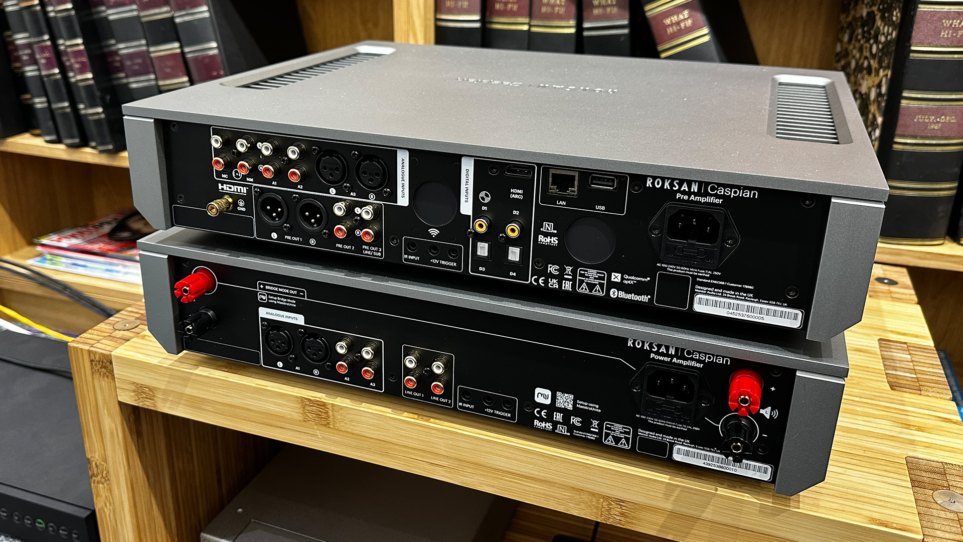 Roksan Caspian 4G Streaming Pre-Amplifier/Caspian 4G Power Amplifier on wooden hi-fi rack in front of bookcase, rear of units showing connections
