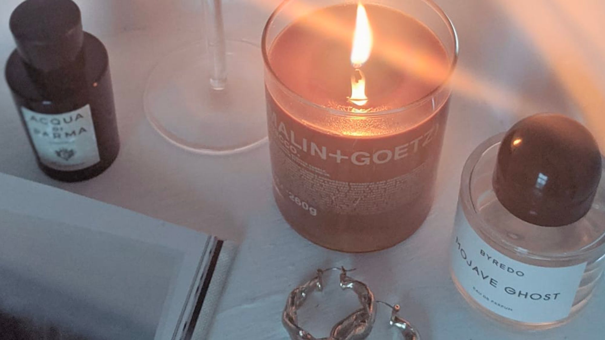 Best Autumn Candles: Malin & Goetz Tobacco candle burning alongside a glass of red wine and a bottle of Acqua di Parma perfume