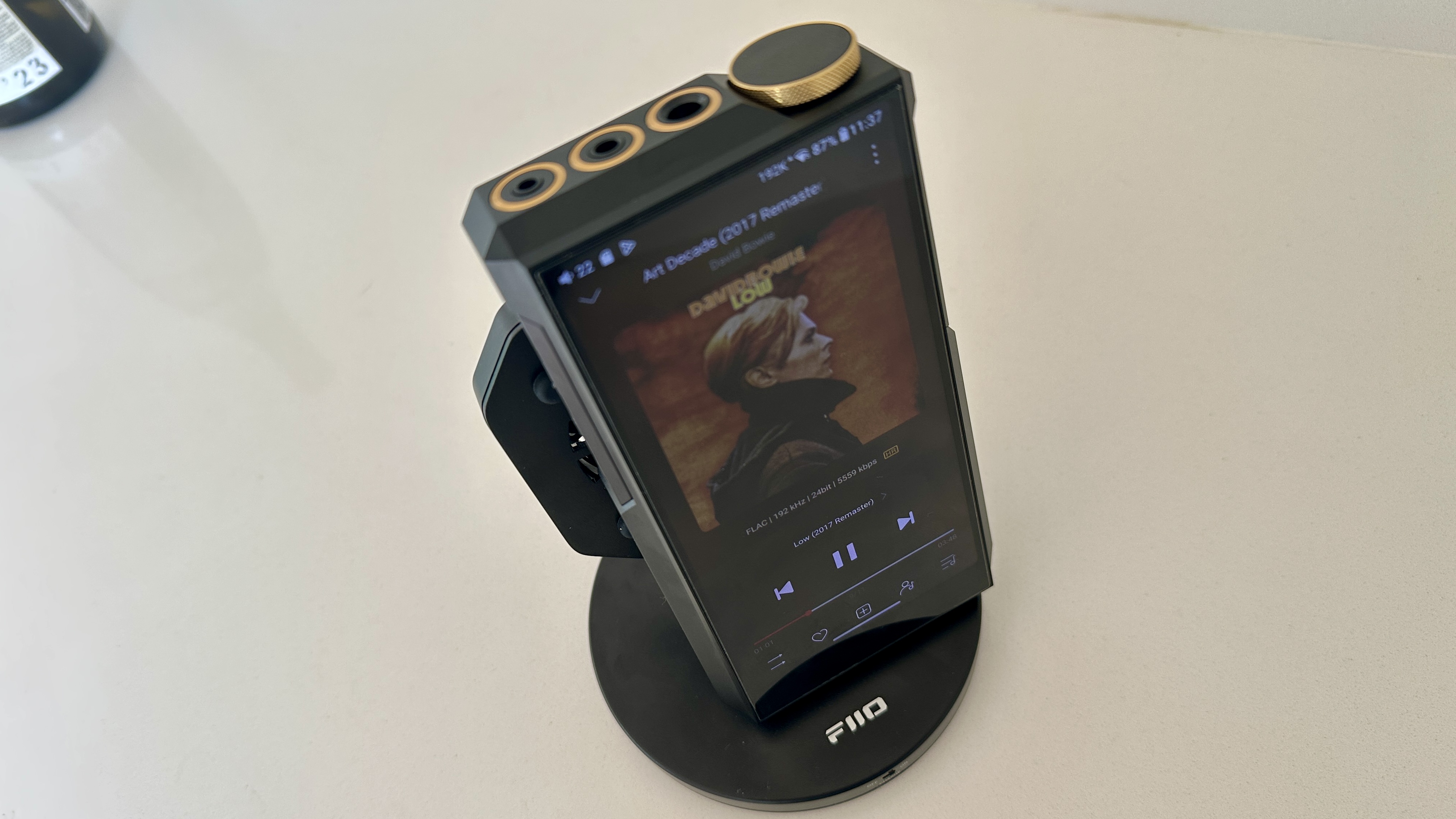 The FiiO M27 player with screen and dial showing, and content on the screen, on beige or yellow background