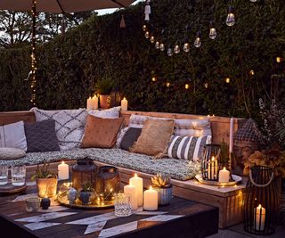 A wooden outdoor corner sofa with boho style cushions and garden lighting with solar candles and parasol lights