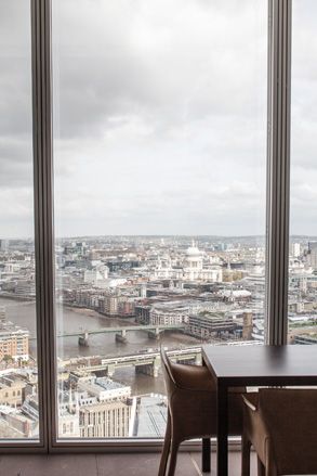 Oblix, London, UK. A table and chairs next to a large window with a view of the city below.