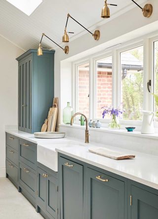 blue Shaker kitchen with white worktops and brass kitchen tap and brass wall lights