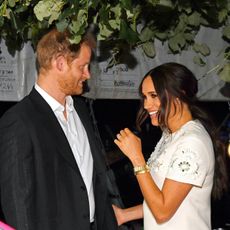 Prince Harry and Meghan Markle smile at each other under a tree