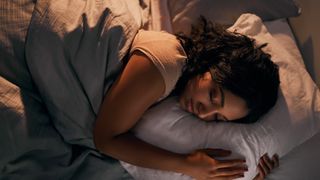 How to fall asleep faster at night: A woman with dark curly hair hugs a white pillow during sleep
