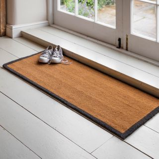 hallway mat right by doors to the outside, with a pair of gray trainers on it, sat on top of white wooden floors