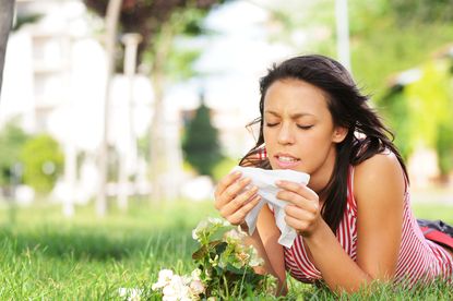 A woman lays in a grassy field, blowing her nose