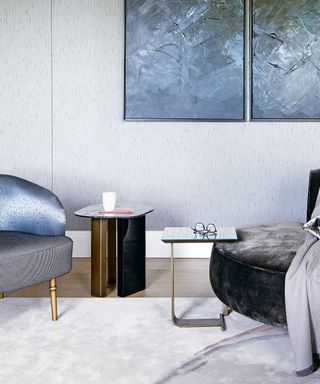Modern living room with two sleek side tables, large artwork on wall, blue velvet lounge chair