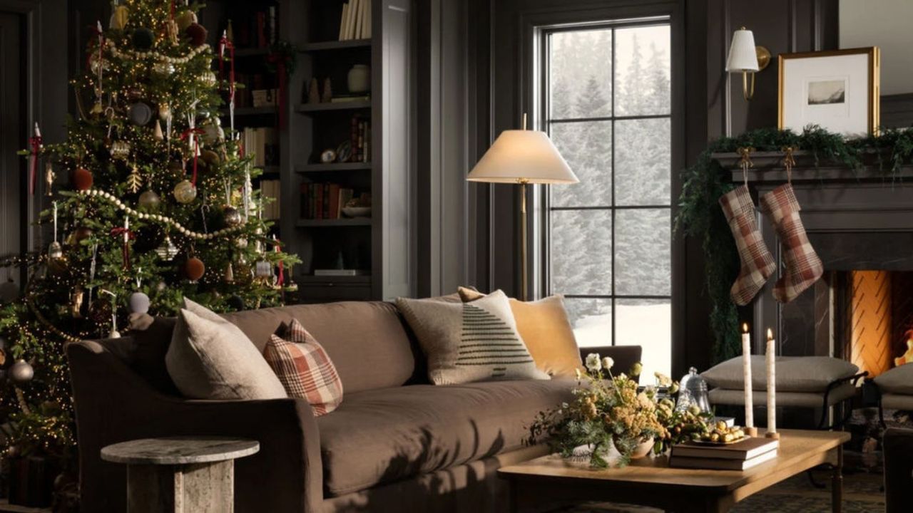 A Christmas tree in a large living room with a sofa and a fireplace, plus windows looking onto a snowy scene.