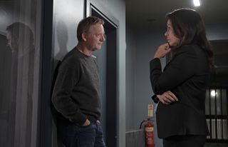 DI Jimmy Perez (Douglas Henshall) and Rhona Kelly (Julie Graham) stand in the corridor outside the interview room in the police station. Perez is leaning back against the wall with his hands in his pockets and a slightly glum look on his face, while Rhona has her chin resting on one hand.