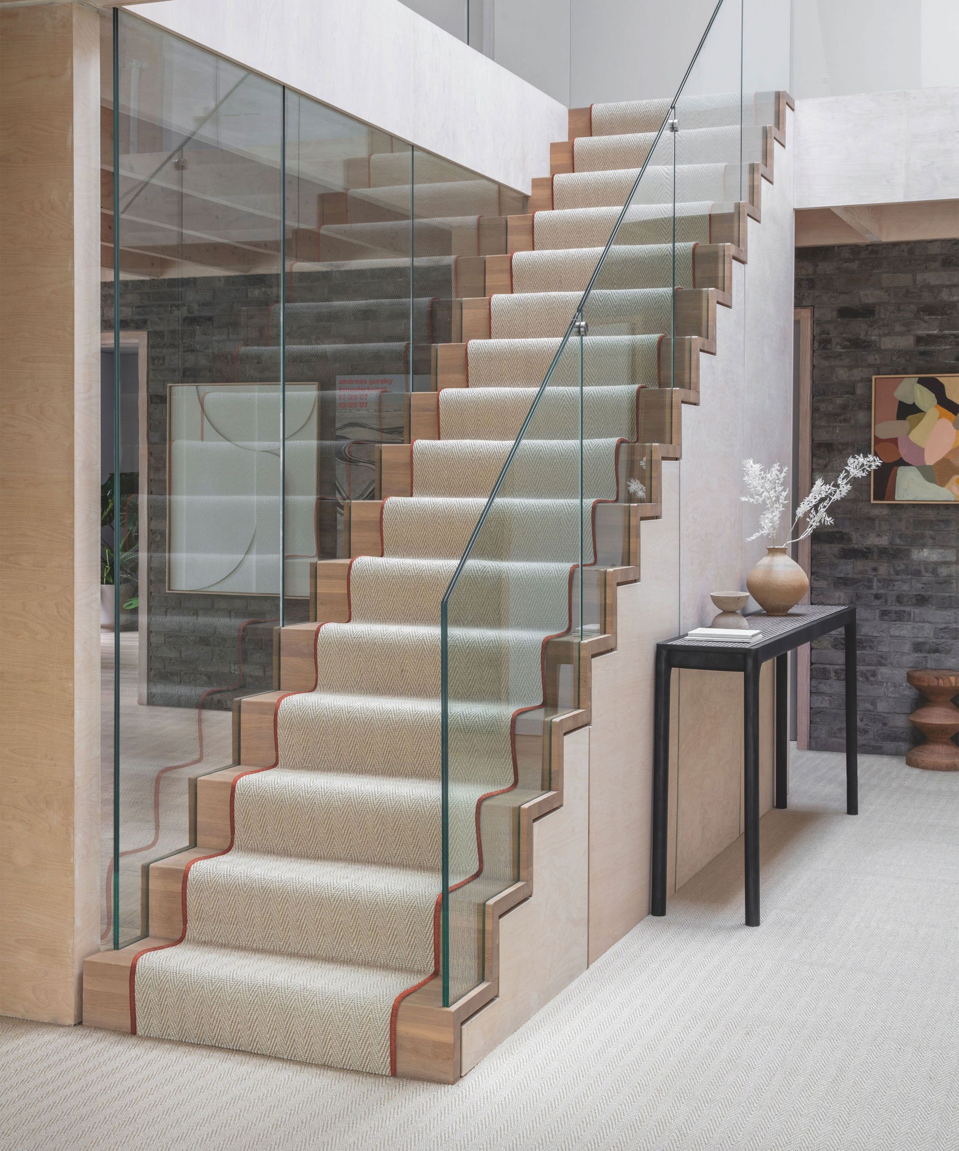 Modern entryway with wood and glass staircase, cream carpet runner and carpet, black console table