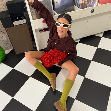 Fashion influencer Vicky Montanari wearing a suede burgundy jacket styled with a red clutch, butter yellow sunglasses, olive green socks, and brown suede boat shoes.