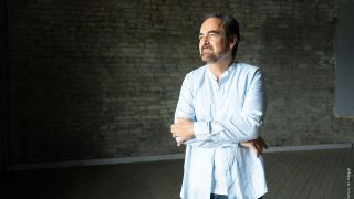 Neal Morse in a blue suit standing by a wall