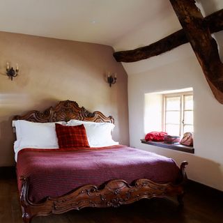 bedroom with white and cream wall wooden beam on wall and wooden bed with designed cushion and brown flooring