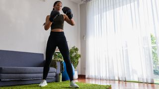 Woman wearing boxing gloves standing in living room, shadow boxing at home