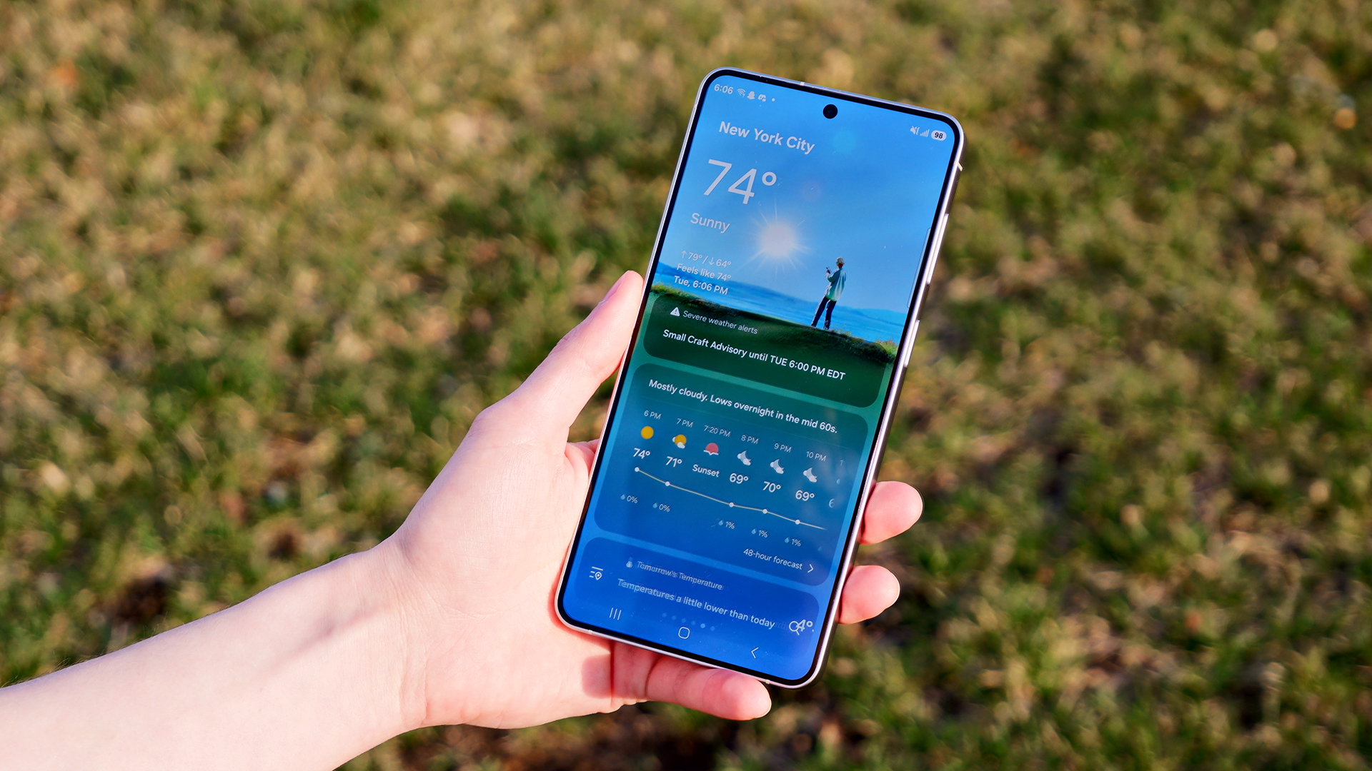 The weather app on the Samsung Galaxy S26 Plus against a grass background.