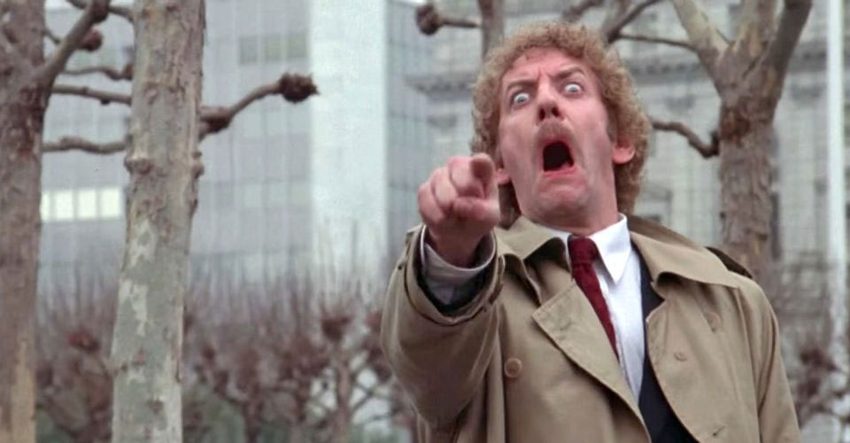 Donald Sutherland mira aterrorizado apuntando a la cámara en un fotograma de La invasión de los ladrones de cuerpos
