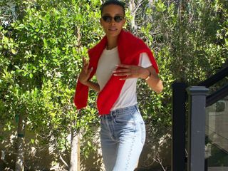 American fashion influencer Tylynn Nguyen poses in a white T-shirt, black wire-rim cat-eye sunglasses, red sweater over the shoulder, and classic jeans