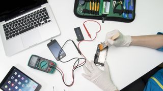 An independent technician repairing an iPhone on a desk alongside other Apple products
