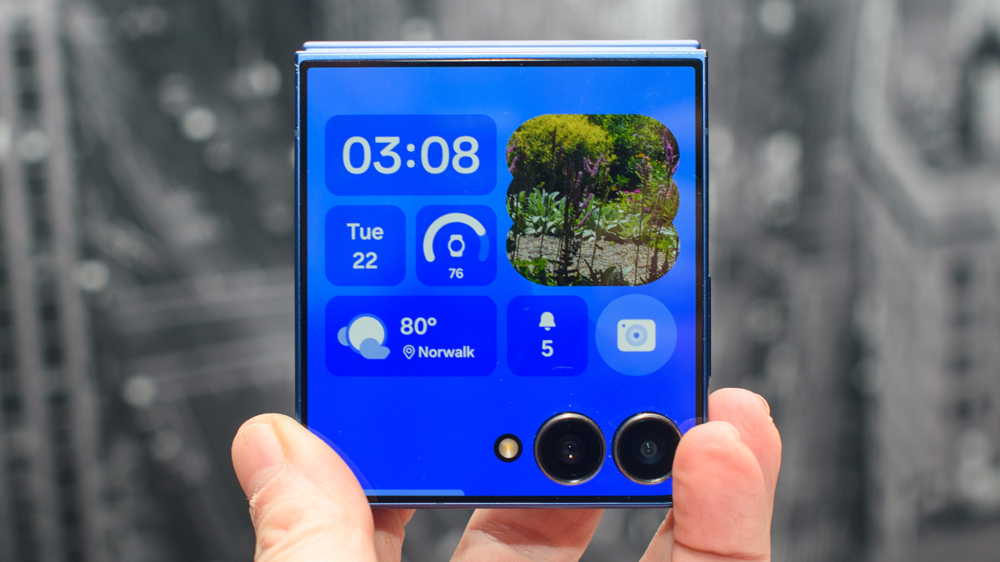 Samsung Galaxy Z Flip 7 in blue in hand showing basic widget info. onthe cover display