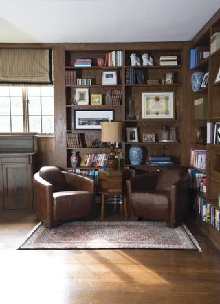 Home library with corner dark wood bookshelves, leather chairs, wood floor and neutral patterned rug
