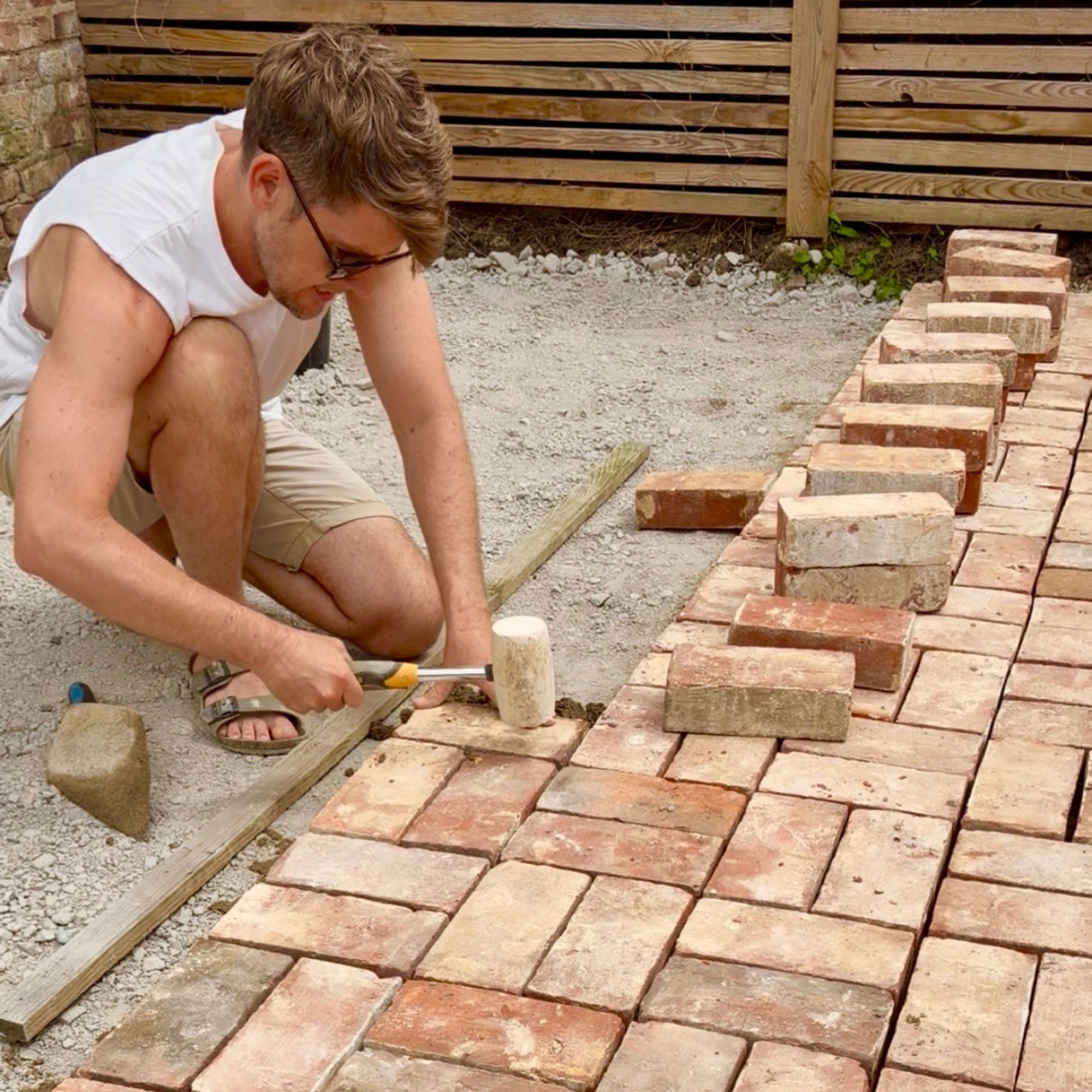 Man hammering in bricks to create patio floor in garden