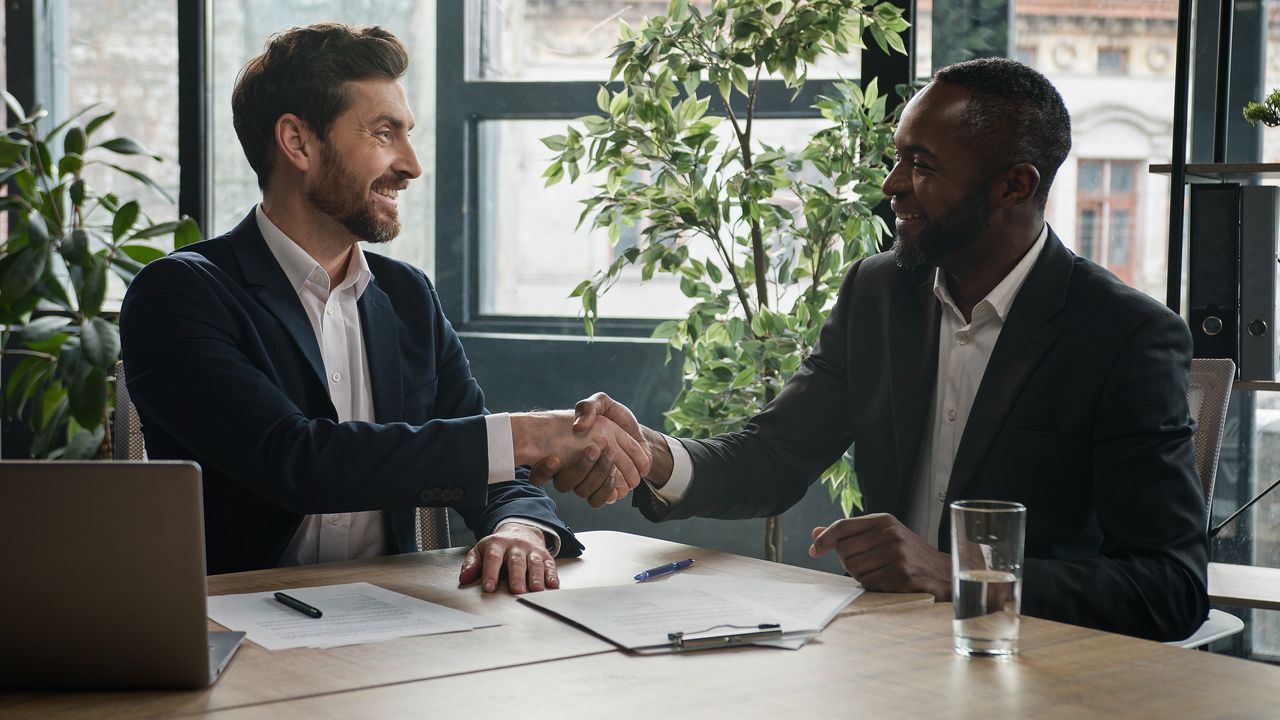 A financial planner shakes hands with his new client at a table in an office.