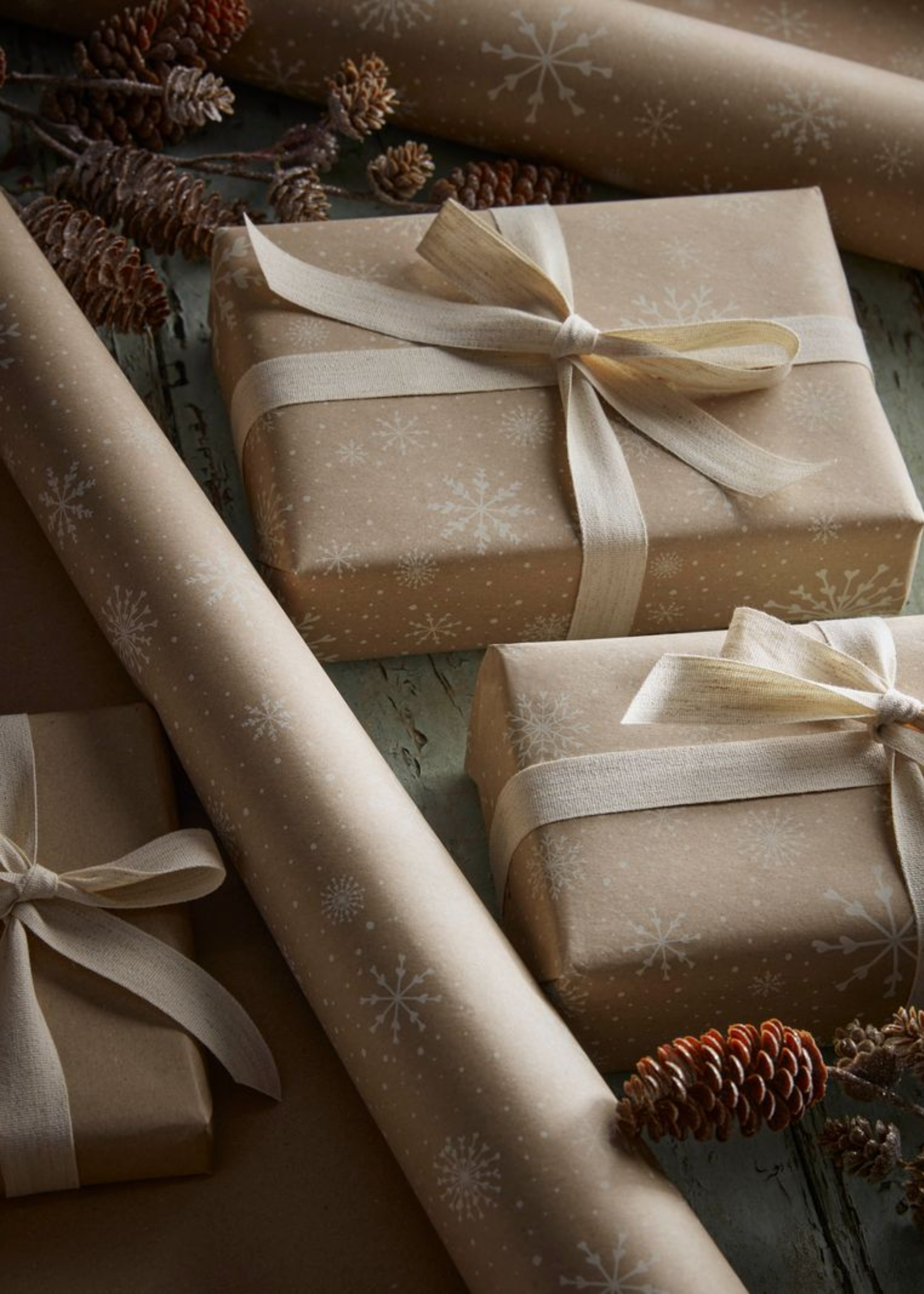 A close-up of presents wrapped in beige wrapping paper with white snowflakes and white ribbon by pinecones