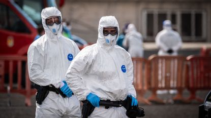 Two people in hazmat suits evacuating the hantavirus cruise ship