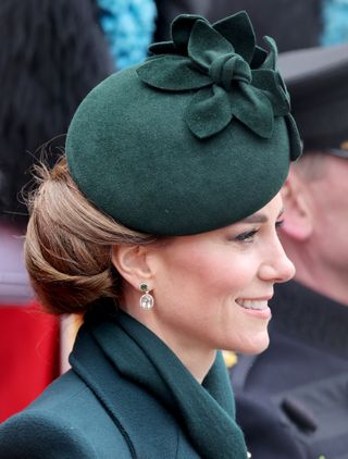 Kate Middleton wearing a green coat and hat turning to the right and smiling