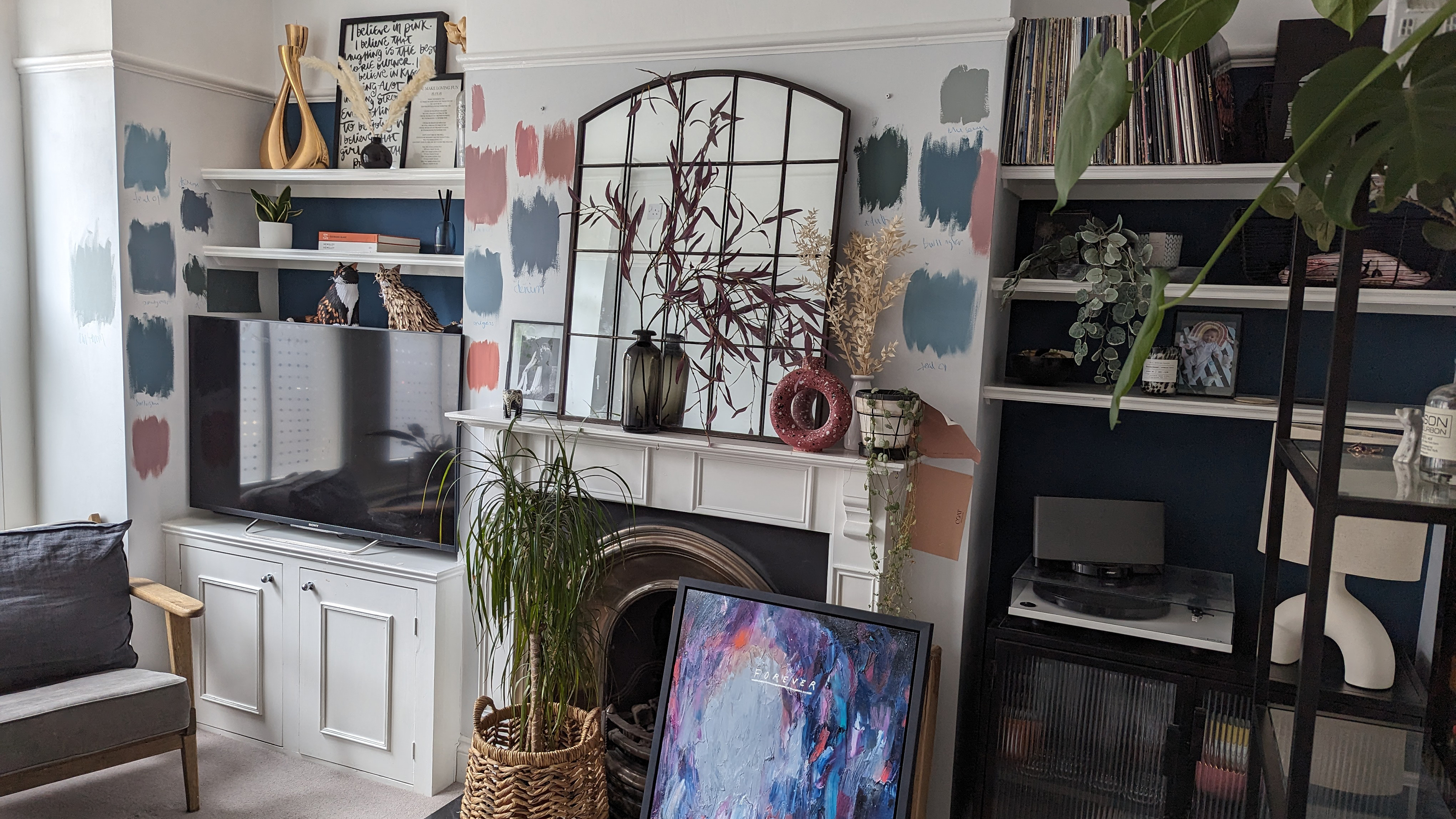 Fireplace in a white living room with built-in alcove unit, showing paint samples on the chimney breast around a framed mirror