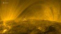 A golden landscape of the sun's surface, featuring looping towers of plasma