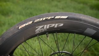 A section of the Zipp 303 wheel with tyre mounted with green grass in the background