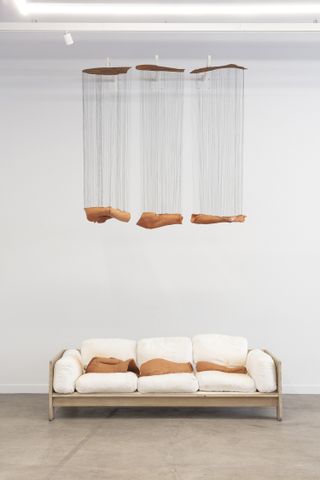 A mid-century modern couch with white leathery cushions sits underneath a floating sculpture of wood and textile.