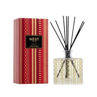 A gold reed diffuser with black reeds, next to a gold and red box