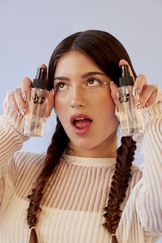 A model stands in front of a plain backdrop holding up two bottles of scent lab fragrance