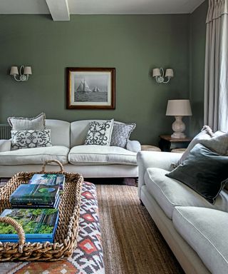 An olive green living room with white sofa, and sisal carpet and Ikat patterned ottoman in a country home.