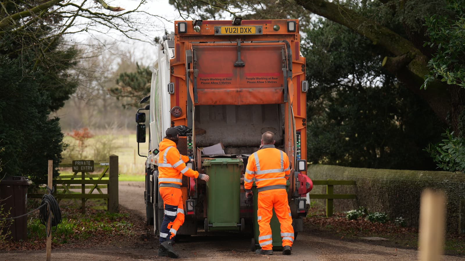 Waste collection workers empty wheelie bins by the entrance to Wood Farm