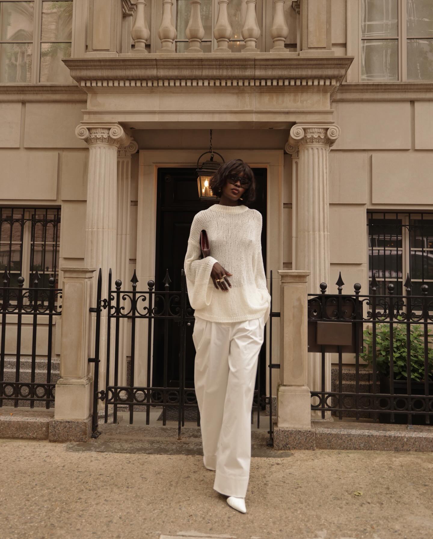 A woman wearing a white sheer knit with white trousers and matching kitten-heel pumps.