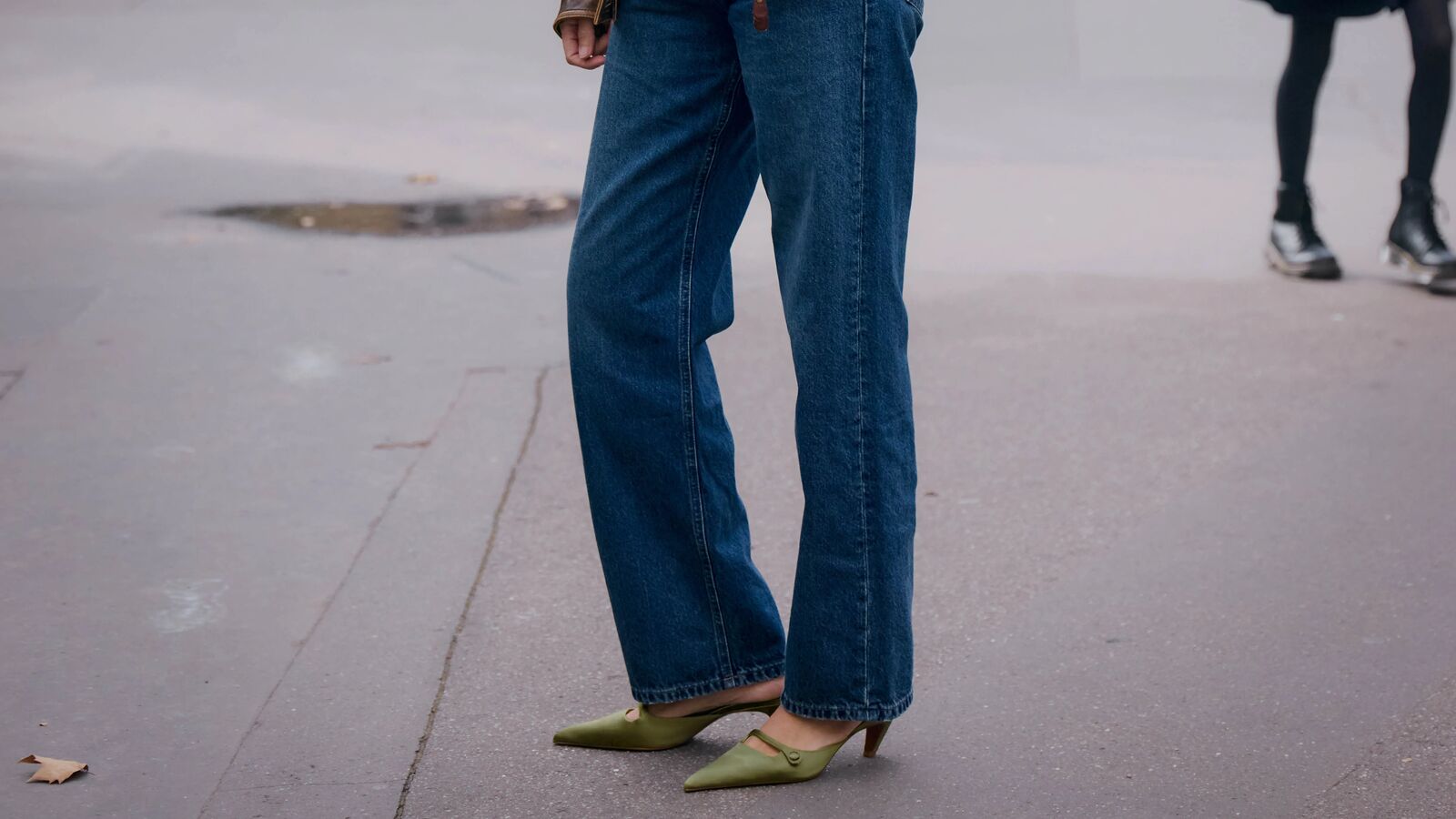 A woman wears blue jeans and green kitten heels.