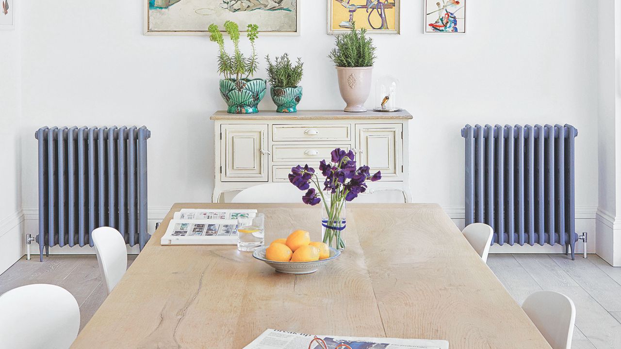 White painted dining room with a wooden dining table, a cabinet against the back wall, and two blue radiators either side of it