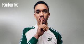 Trent Alexander-Arnold holding his fingers to his lips wearing a cream and green Adidas Originals tracksuit during a photoshoot for the cover of FourFourTwo magazine