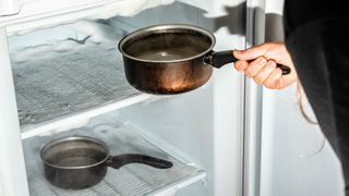 woman placing saucepans filled with water to speed up the process of defrosting the freezer
