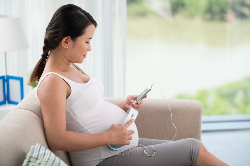 A pregnant woman sits on a couch, holding her phone.